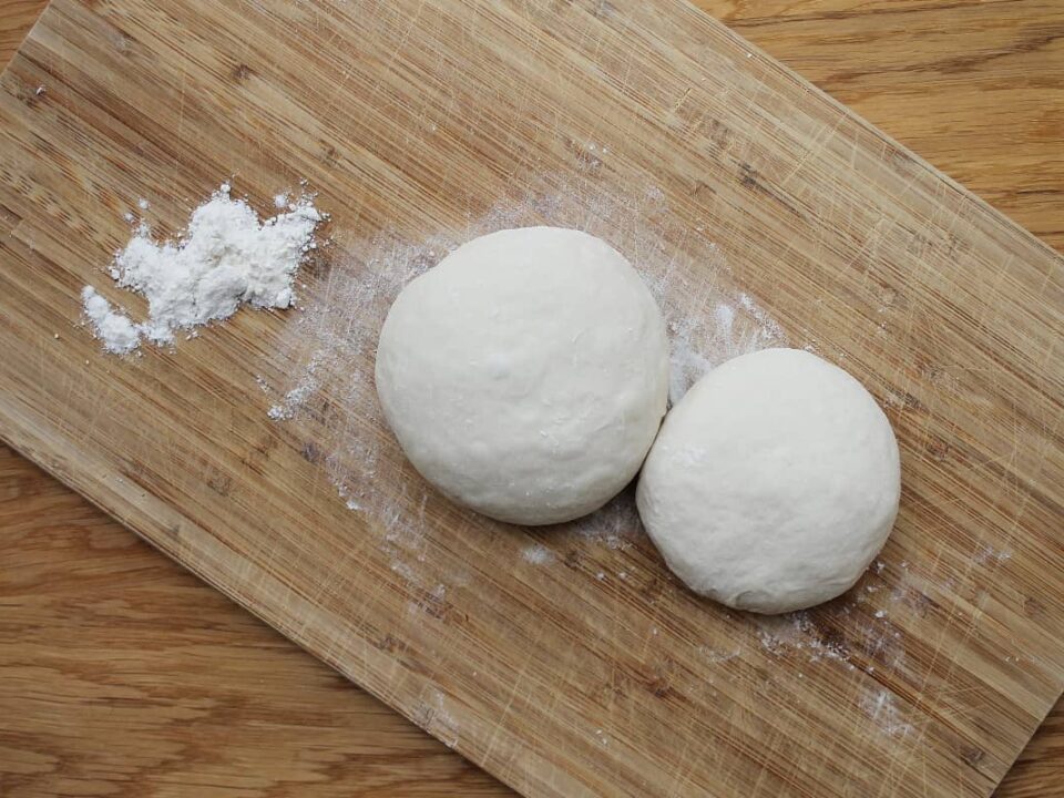 Zwei Pizzateig Ballen auf einem Holzbrett