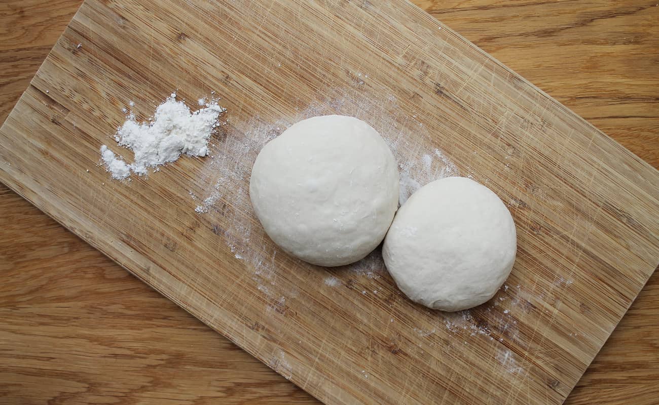 Zwei Pizzateig Ballen auf einem Holzbrett